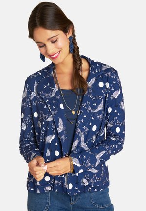 Navy blue jacket with white crane and dot patterns, featuring a tailored design and soft fabric. Worn over a matching top.