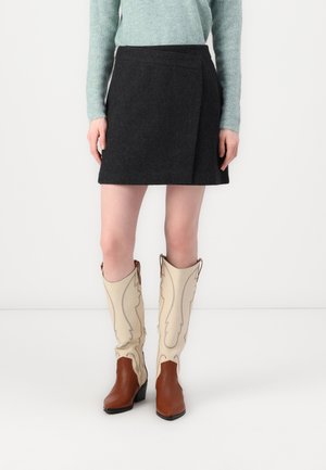 Black skirt with a wrap design, made of textured fabric. Paired with tall beige cowboy boots featuring decorative stitching and brown accents.
