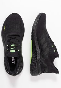 Para czarnych butów do biegania Adidas z teksturowanymi podeszwami, neonowozielonymi oczkami na sznurowadła oraz tkaniną Aeroready, przedstawiona z widokiem z góry i boku.