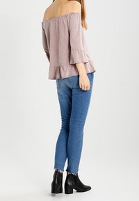 Lichtroze off-the-shoulder top met een ruffled peplum onderrand, gecombineerd met blauwe skinny jeans en zwarte enkellaarsjes. Eenvoudig ontwerp en texturen.