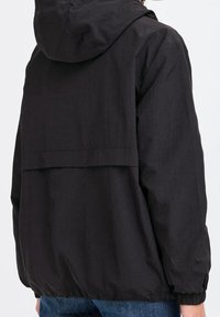 Svart huva jacka gjord av lättviktsmaterial, med en lös passform, elastiska ärmavslut och en längre bakdel för ökad täckning.