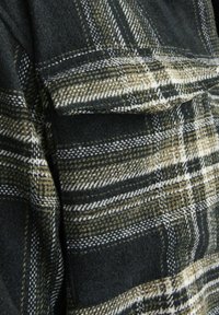 Camasa flanel în carouri, de culoare verde închis, maro și alb, cu un finisaj texturat. Dispune de un buzunar pe piept și un model în carouri stratificat.