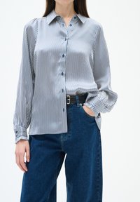 Randig långärmad skjorta i ljusblå och vit satin, med klassisk krage, knappstängning och rynkade manschetter.