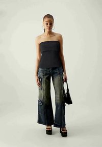 Μαύρο τοπ χωρίς τιράντες, μπλε τζιν με φαρδιές γραμμές και τσέπη με μ patch, και μαύρες πλατφόρμες. Τα αξεσουάρ περιλαμβάνουν μια μικρή μαύρη τσάντα.