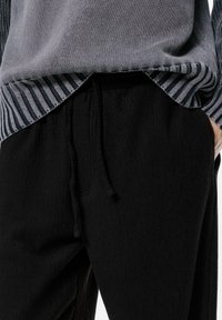 Sweter w odcieniu szarym z paskowanym dołem, zestawiony z czarnymi, prążkowanymi spodniami z elastycznym pasem i detalem sznurkiem. Tkanina o fakturze.