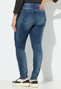 Dopasowane dżinsy w ciemnoniebieskim odcieniu, z wysokim stanem, tylnymi kieszeniami i gładką fakturą. W zestawieniu z czarno-białymi sneakersami.