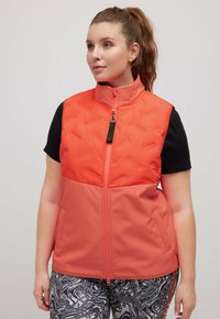 Vadderad väst i klargul och korall, med hög krage, framzipper och två sidofickor. Matchad med mönstrade svarta leggings.