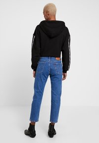 Sudadera negra recortada con capucha, vaqueros de cintura alta azules y botas negras hasta el tobillo, con un diseño minimalista y casual.
