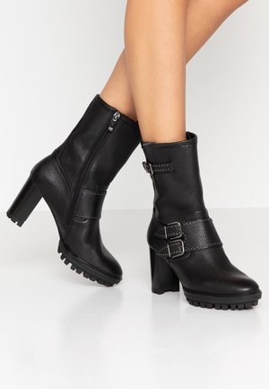 Bottes en cuir noir mi-mollet avec talons épais et semelles crantées, dotées de deux boucles latérales et d'une fermeture éclair sur le côté intérieur.