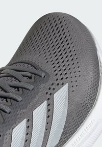 Sive patike za sport sa teksturiranim gornjim dijelom, prozračnom mrežicom i reflektirajućim srebrnim detaljima. Imaju klasične vezice i gumeni potplat.