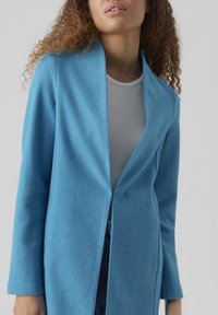 Ljusblå kappa i ullblandning med sjalkrage, öppen fram, och långa ärmar. Slät textur och skräddarsydd passform.