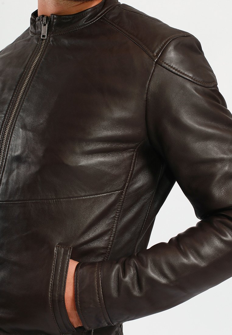 Chaqueta de cuero marrón con un diseño ajustado, que presenta un cuello alto, cierre de cremallera y bolsillos laterales. Textura suave y detalles de costura mínimos.