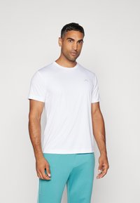 Fehér, rövid ujjú sportpóló, kerek nyakkivágással és egy diszkrét logóval a mellkason, világoskék sportnadrággal párosítva.