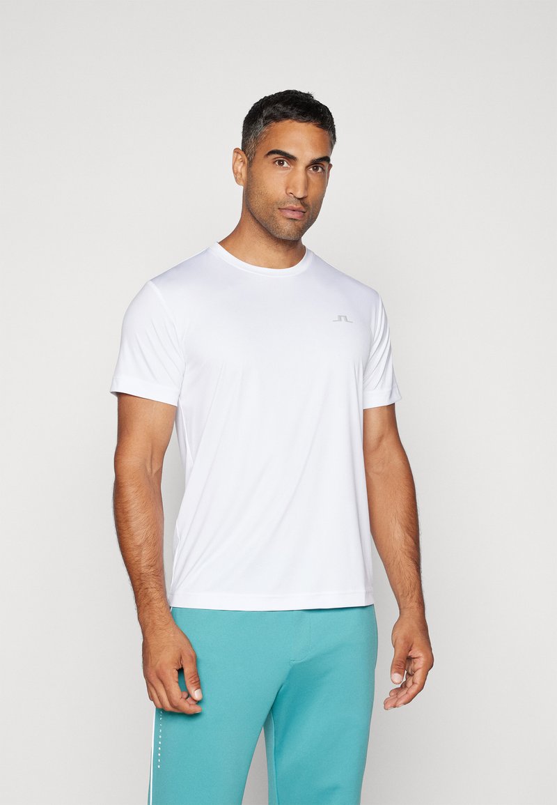 Fehér, rövid ujjú sportpóló, kerek nyakkivágással és egy diszkrét logóval a mellkason, világoskék sportnadrággal párosítva.