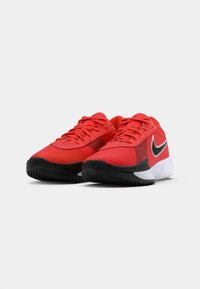 Røde atletiske sneakers med en mesh-overdel, sorte accenter og en tekstureret sål; har et fremtrædende sort swoosh-logo på siden.