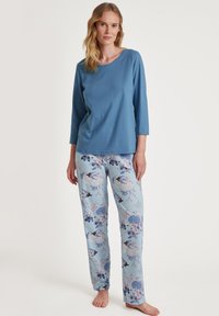 Blauw longsleeve top met een ronde hals, gecombineerd met lichtblauwe broek met bloemenpatroon en ingewikkelde ontwerpen in paarse en blauwe tinten.
