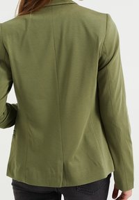 Olivgrön kavaj med en figursydd form, som har en enda slits bak och en slät yta. Inkluderar axelsömmar och minimalt med detaljer.