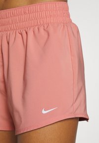 Růžové sportovní šortky s elastickým pasem, hladkou texturou a bílým logem Nike na lemu. Vyznačují se čistým šitím a přiléhavým střihem.