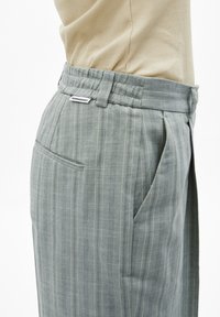 Grijs gestreepte broek van een gestructureerde stof, met een tailleband en zijzakken. Merkenlabel zichtbaar boven de tailleband.