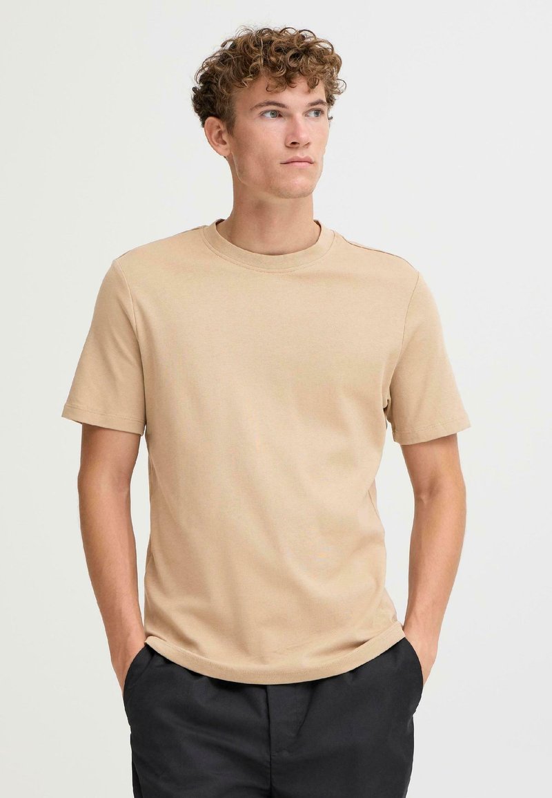 Beige short-sleeve t-shirt made of cotton with a round neckline and a smooth texture, displayed on a model against a neutral background.