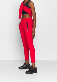 Rode joggers met een slim fit, voorzien van een zwarte ritszak, geribbelde boorden en een geborduurd logo. Gelijk gedragen met een zwarte crop top en schoeisel.