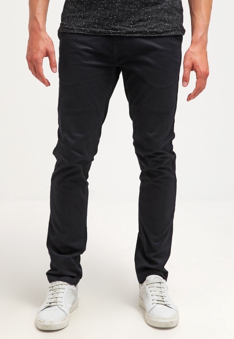 Schwarze Slim-Fit-Chinos aus Baumwolle, mit glatter Textur und subtiler Eleganz, kombiniert mit weißen Sneakers für einen Kontrast.