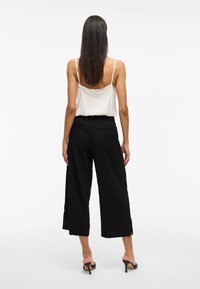 Pantalones negros de pierna ancha con aberturas laterales y un corte relajado, combinados con una camisola de satén blanca con un escote adornado con encaje.