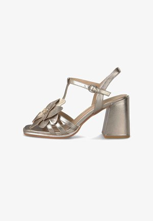 Metaliczne srebrne sandały na wysokim obcasie z paskiem typu T, klamrą przy kostce, szerokim obcasem oraz dużym dekoracyjnym kwiatem na przednich paskach.