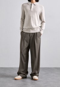 Polo en maille beige avec une patte de boutonnage à cinq boutons, associé à un pantalon large plissé gris et des baskets de couleur claire. Tissus texturés.