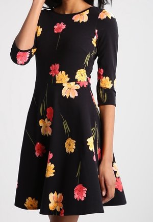 Robe noire avec une jupe évasée ornée d'un imprimé floral en rose, jaune et orange. Elle a des manches trois-quarts et un col rond.