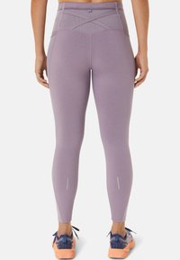 Lila hochtaillierte Leggings mit einem Kreuzdesign auf der Rückseite und reflektierenden Akzenten in der Nähe der Knöchel. Glattes, dehnbares Material.