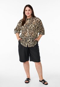 Chemise à imprime léopard avec manches retroussées, assortie à un short noir à mi-cuisse et des sandales noires à glissière avec des accents cloutés.