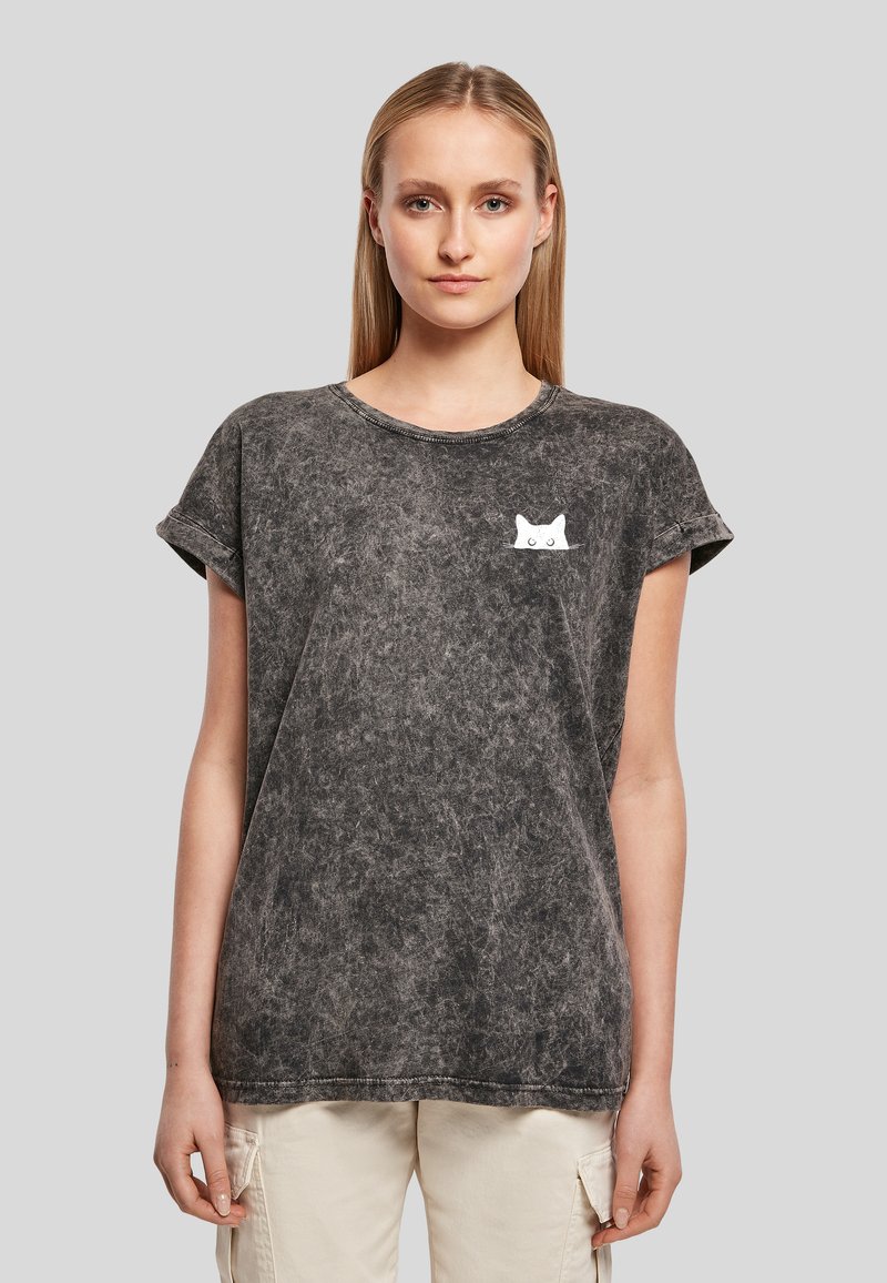 Jeune femme portant un T-shirt gris effet délavé avec un petit motif de visage de chat blanc sur la poitrine gauche et un pantalon cargo beige.