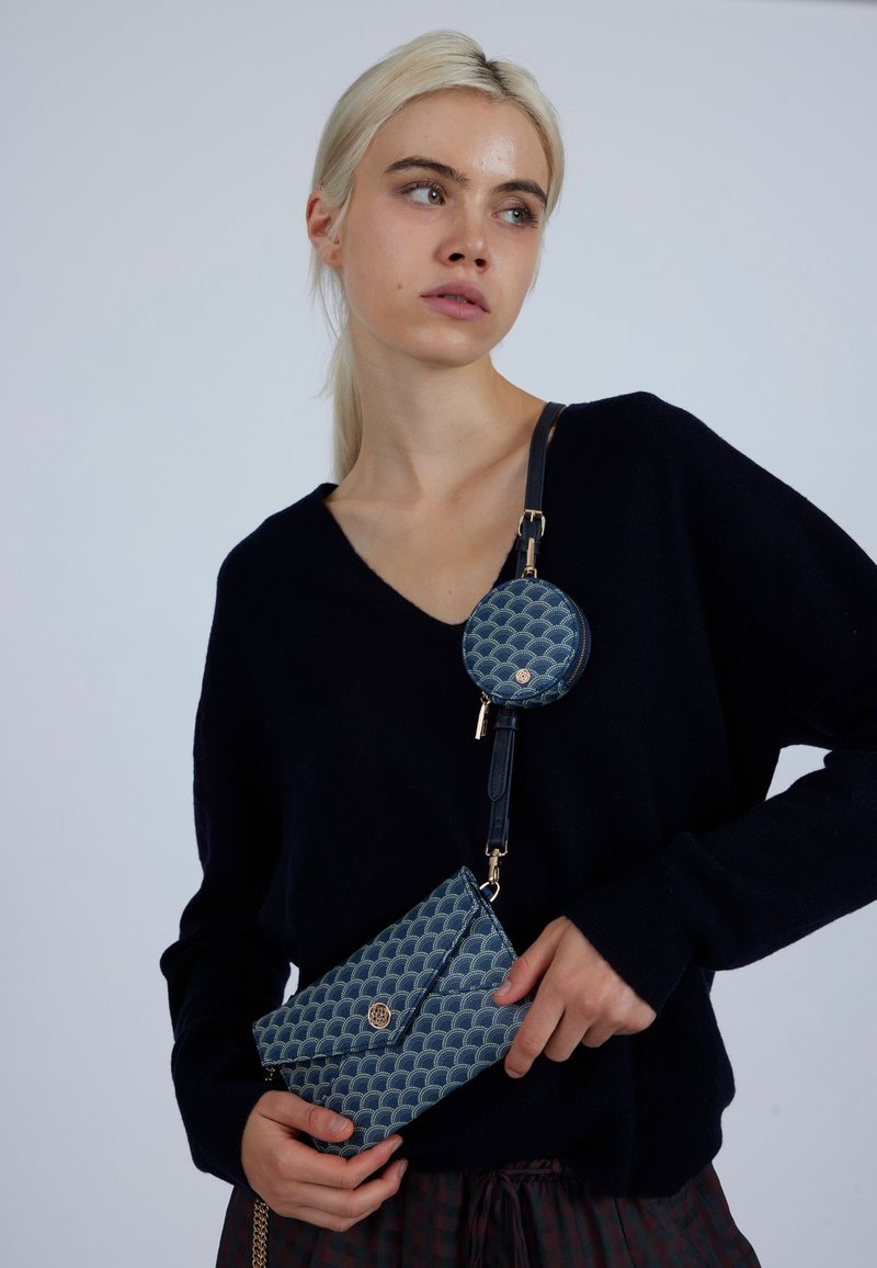 Modrá prošívaná kabelka se vzorem mušle, zlatým kováním, odnímatelnou kulatou kapsou a černým popruhem; vyrobená z texturovaného materiálu.