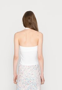 Top halter branco com um design ajustado, textura suave e comprimento cropped, usado com uma saia de padrão floral.