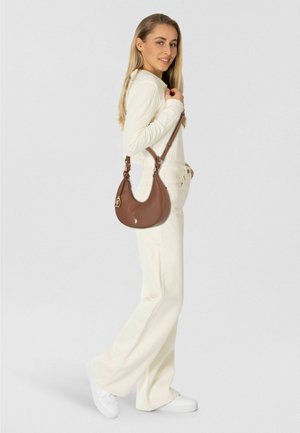 Bolso de hombro de cuero marrón con forma curva y correa ajustable, con un acento de logotipo metálico. Usado de manera casual con un conjunto color crema.