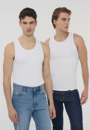 Top in cotone bianco indossati da due modelli. Un modello in jeans chiari, l'altro in jeans scuri. Design semplice, senza motivi.