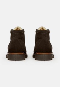 Botines de ante negro con un acabado texturizado, suelas de goma y un forro de color claro que contrasta, presentando una punta redondeada y costuras sencillas.