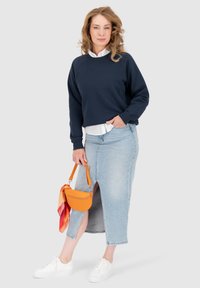 Felpa navy, camicia bianca col colletto, gonna in denim azzurro con spacco laterale, borsa arancione, sneakers bianche. Outfit casual con livelli di texture.