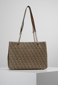 Tote taška s monogramem v béžové a hnědé barvě, s dvojitými ramenními popruhy a řetízkovými akcenty. Hladká textura, strukturovaný tvar.