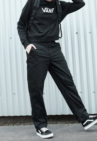 Felpa nera con logo bianco "VANS", abbinata a pantaloni neri e sneakers in bianco e nero. Tessuto strutturato e vestibilità comoda.