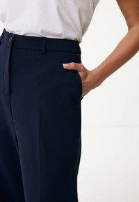 Marineblauwe broek gemaakt van lichtgewicht stof met een zachte textuur. Bevat een voorzak, riemlussen en een knoopsluiting.