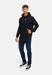 Sort hoodie med en frontlomme, struktureret materiale, snøre detaljer, kombineret med mørkeblå jeans og moderne sneakers.