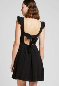 Robe noire sans manches avec un col froncé, un dos nu et un lien en tissu à la taille. Texture douce avec une jupe fluide.