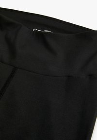 Leggings atletici neri con una texture liscia, vita alta e dettagli di cucitura a contrasto. Design semplice senza ulteriori motivi o accenti.