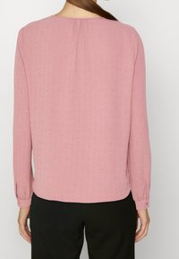 Långärmad blus i mjuk rosa tyg, med rund halsringning, knäppta manschetter och subtil textur. Skräddarsydd passform med en något rundad nederkant.