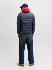 Marineblauwe pufferjack met een rode capuchon, gestructureerde stof, achterkant gezien. Gecombineerd met losse blauwe jeans en beige schoeisel, een blauwe muts maakt de look compleet.