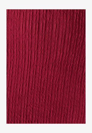 Guban tkanina v globoko rdeči barvi, s teksturirano površino, ki ima navpične črte in rahle razlike v globini, kar ustvarja dinamičen vizualni učinek.