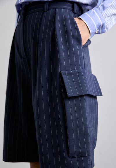 Shorts bleu marine à rayures, en tissu tissé, avec une poche cargo sur le côté avec rabat, coupe ajustée et plis structurés.
