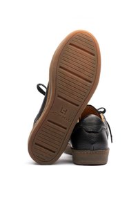 Schwarze Lederschuhe mit strukturiertem Finish, Gummisohle mit horizontalen Rillen und Markendetail "Lactae Hevea" auf der Außensohle.